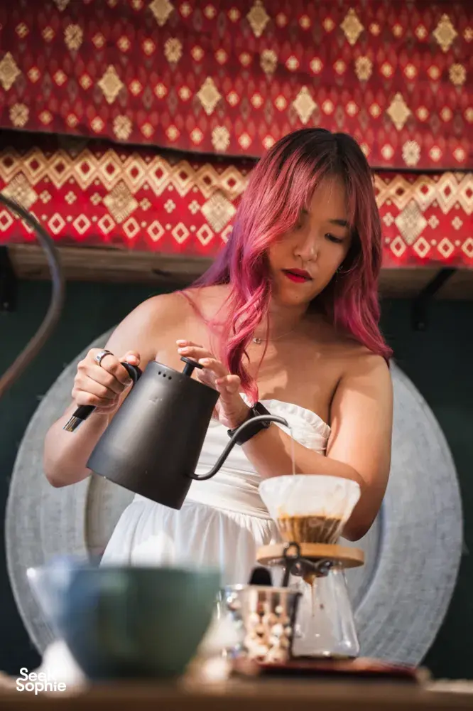 Woman with pink hair pouring coffee into a brewer during hands-on coffee roasting and bagel brunch workshops in Singapore