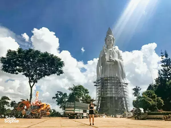 Large white Buddha statue rising from scaffolding in a temple courtyard under bright skies near Da Lat during the Easy Rider trip