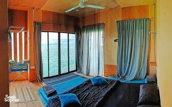 Sea lodge bedroom in Semporna with a double bed, blue curtains and floor-to-ceiling windows looking out to the ocean