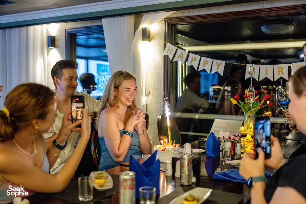 Birthday party on the Oasis Bay Party Cruiser with friends at a candlelit table, celebrating together on Halong Bay