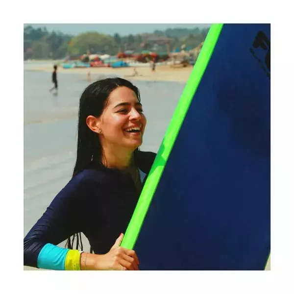 Smiling surfer in a wetsuit grips a green surfboard fin at a Weligama beach during a training session