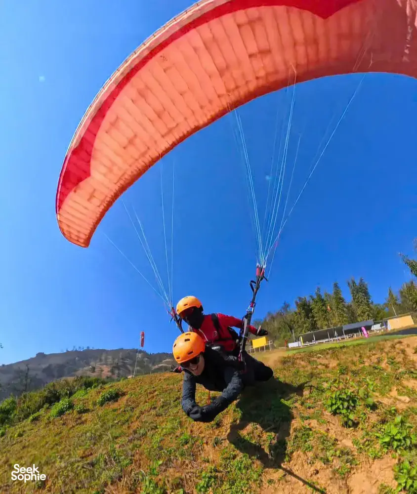 Tandem paragliders suspended under a red canopy above terraced valleys, preparing for lift-off in Vietnam Sapa