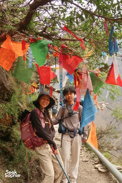 Trekking on the Tiger Leaping Gorge trail in Lijiang with colourful prayer flags overhead as hikers climb a rocky path