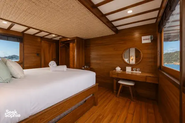 Travass Life phinisi cabin with a double bed, pillows and bedside lamps for a Komodo shared trip, Labuan Bajo