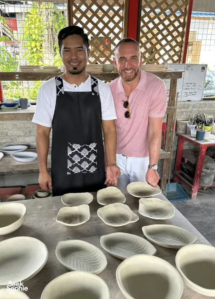 Two hosts and visitors at Ilham Ceramic Studio in Langkawi standing by finished ceramic pieces on a worktable