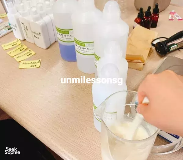 Hand pouring milky mixture into a clear cup as collagen skincare bottles line the table at a Korean workshop in Singapore