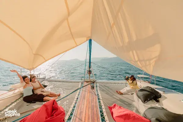 Travellers lounging under the sail canopy on SY Mawali catamaran while cruising from Kota Kinabalu