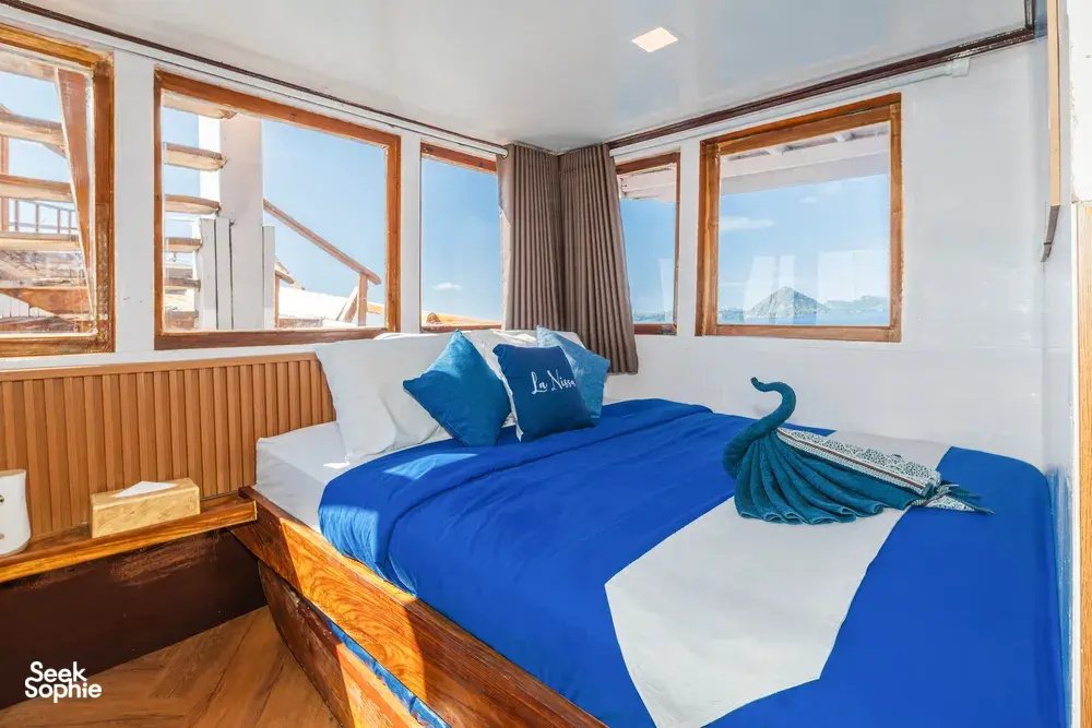 La Famille cabin on the Komodo boat with a blue bed, window views and a folded-towel swan, for 3D2N stays in Labuan Bajo