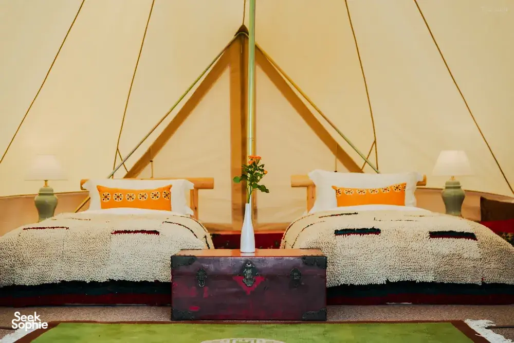 Cozy glamping tent interior at Ferme Liotard in Shangri-La with two beds, patterned cushions and a rug