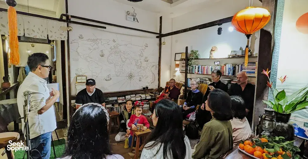 Seorang fasilitator menunjuk dinding bagan kelahiran sementara sekelompok kecil mendengarkan di workshop Chan Dat Living Room, Hoi An