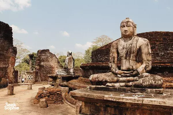 Large seated Buddha statue on a stone plinth beside ruined walls and pathways, part of Polonnaruwa’s ancient temple grounds