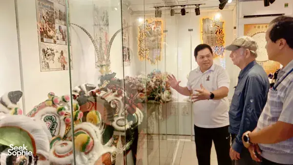 Visitors learn about lion dance traditions as a guide gestures beside a glass case of ornate lion heads in a Ho Chi Minh City museum