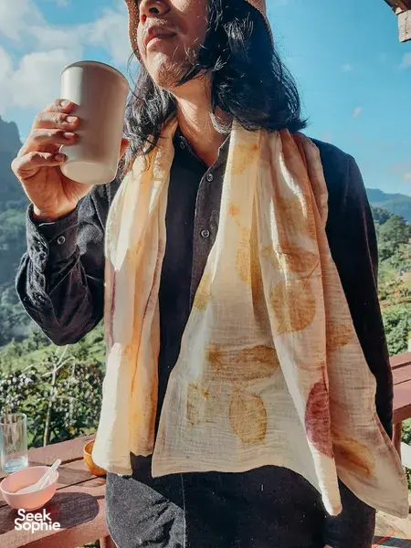 Participant holding a cup wearing a botanical eco-dyed scarf, taking a break during Dip-Dye By Noo’s session near Chiang Mai