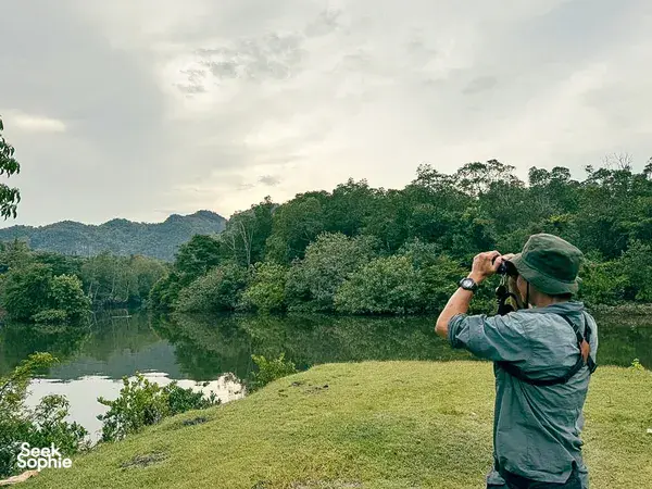 Nature lover photographing over a calm lake bordered by green hills and forest in Langkawi during a guided birdwatching stop