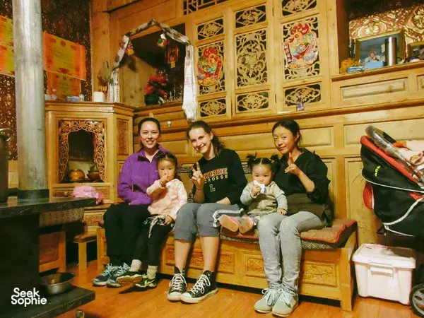 Family gathering indoors in a Tibetan homestay in Shangri-La, with two adults and two children smiling on a bench