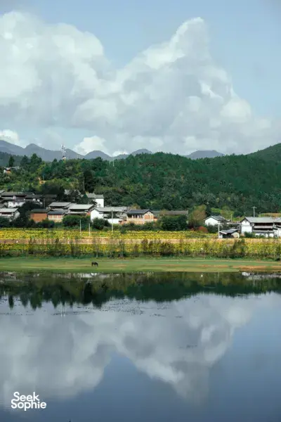 Shaxi riverside village in Dali, Yunnan, with a calm lake reflecting rooftops and forested mountains during the eco retreat