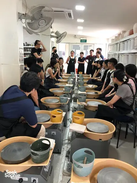 Sesi tembikar roda putar di studio Singapura, dengan pasukan kreatif berkumpul mengelilingi roda seramik — bengkel di Singapura