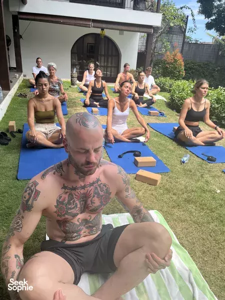 Man in the foreground practices a yoga pose while a group sits quietly on mats during a private villa wellness session in Bali, Canggu