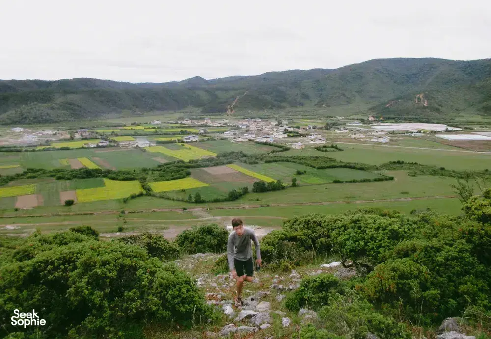 Scenic view over fields and the village of Shangri-La from a rocky hillside, with a traveller looking out