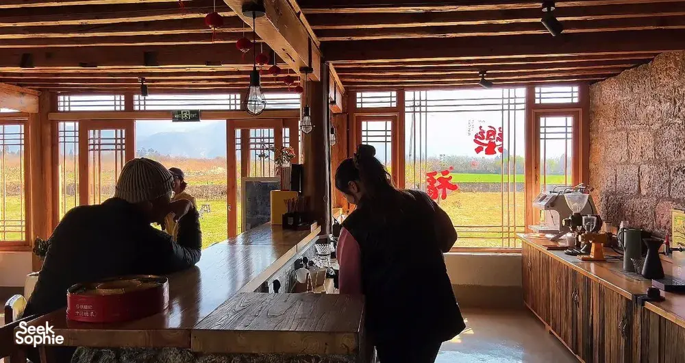 Silhouetted guests learning about Yunnan coffee at a family workshop in Lijiang, seated by large roasting and brewing counter