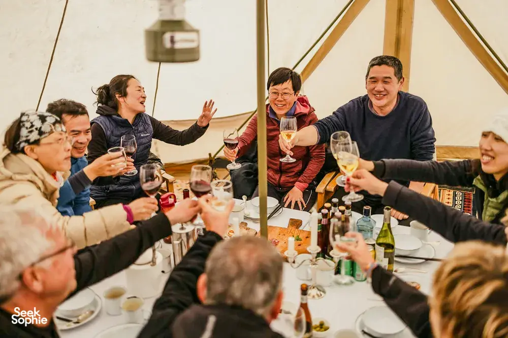 Group dining and toasting in a canvas dining tent during a nomadic caravan camp in Shangri-La’s remote valleys