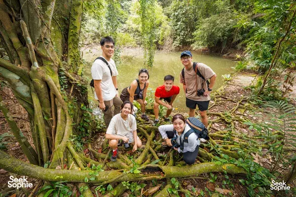Kneeling hikers on forest roots during a Mount Faber hike, smiling in greenery with a Sneak-Peek Singapore group, Singapore hidden gems
