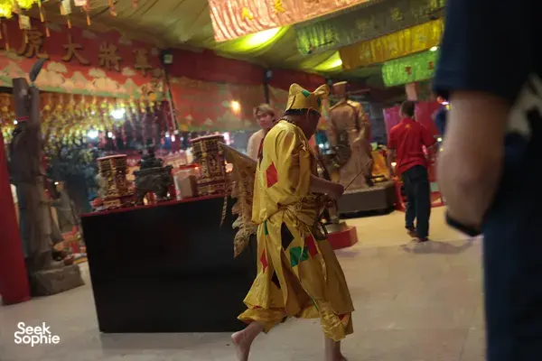 Ritual performer in a yellow ceremonial robe walking through a decorated Chinese temple corridor during a night guided ritual in Singapore