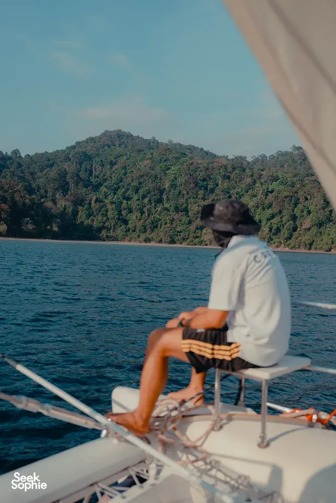 A traveller relaxing on SY Mawali catamaran, watching lush green coastline drift by near Kota Kinabalu