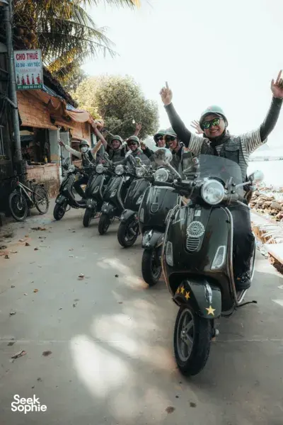Line-up of Vespas with helmeted riders on a roadside lane near Hoi An, ready for hidden village stops and lunch