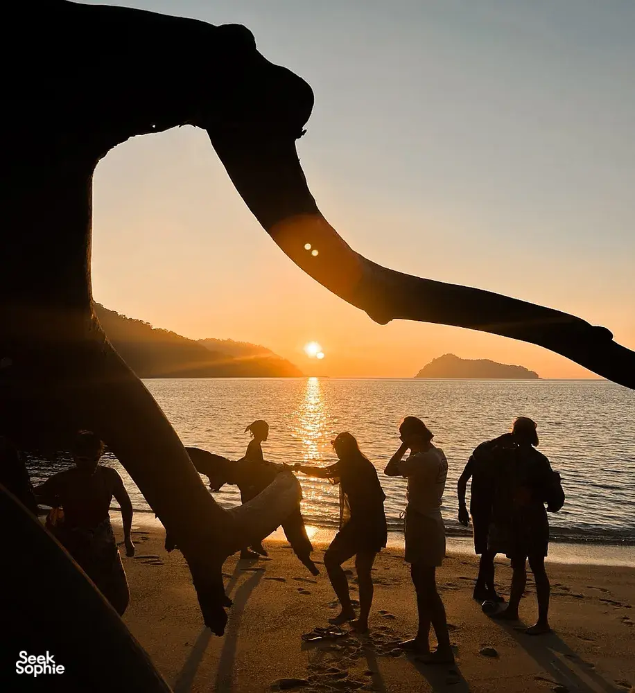 Silhouetted group walking along the beach at sunset, with a sail-like hand in the foreground, at Surin Island, Khao Lak