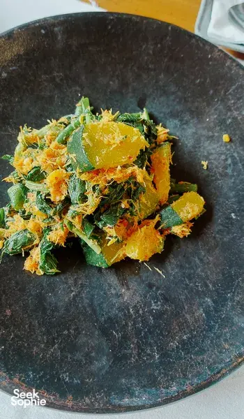 Chopped leafy greens with orange veg piled on a dark ceramic plate during a traditional Manggarai vegan cooking class in Labuan Bajo