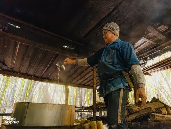 Worker at Tanoti Crafts in Kuching pours palm sap beneath the stilt-house roof, filling jars for the palm sugar process