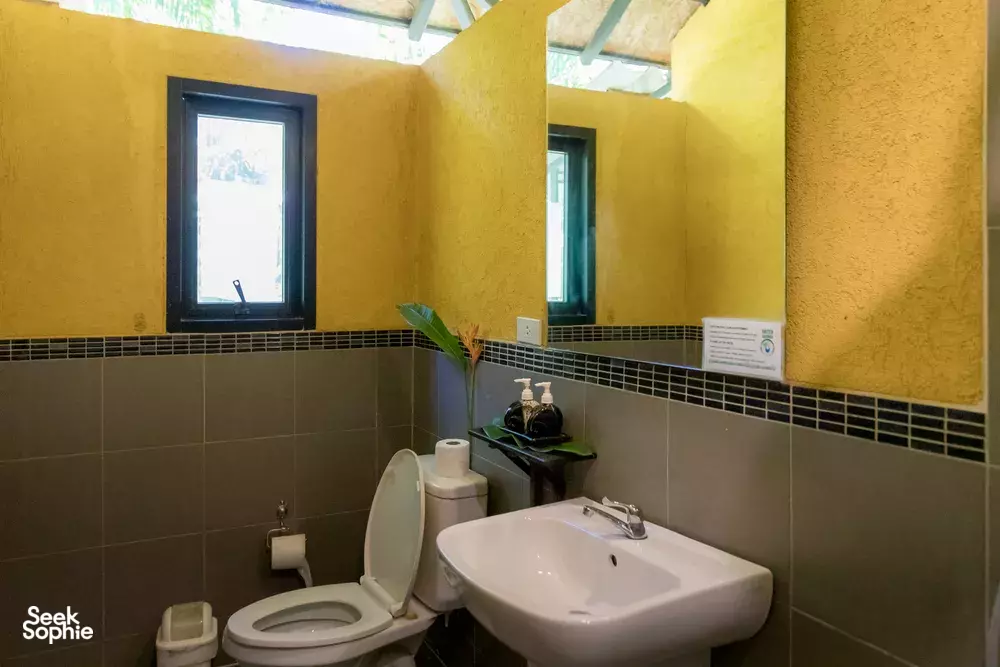 Clean lodge bathroom with toilet and white basin, set inside a bright room at Anurak Lodge in Khao Sok National Park