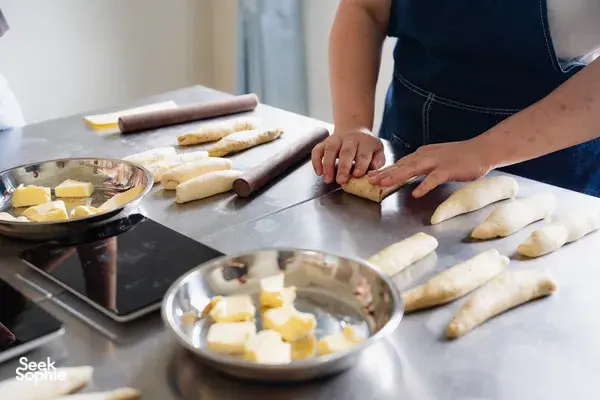 Hands shaping shio pan dough on a metal bench beside a bowl of butter at a bread-making session—workshops in Singapore