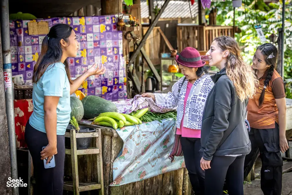 Participants sort fresh vegetables on an outdoor prep table during a Mae Kampong forage-to-table cooking class in Chiang Mai
