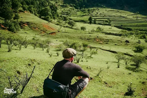 Traveller sitting on a grassy lookout above terraced countryside around Lijiang, Yunnan, on a Yi and Naxi village trek