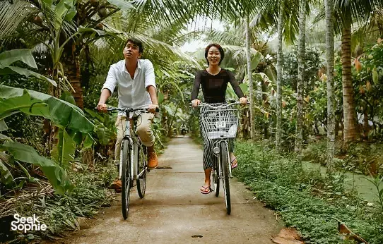 Bike trip in Ben Tre from Mỹ Tho with two cyclists pedalling along a palm-lined path in Vietnam’s Mekong Delta
