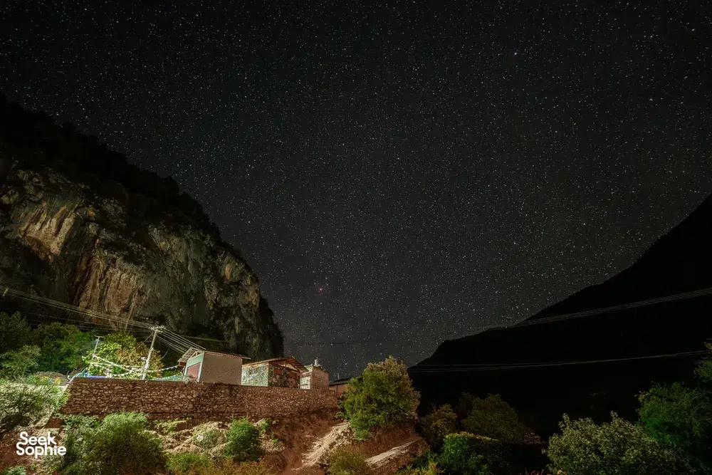 Starry night sky over Shangri-La mountains and valley village rooftops with power lines below at night