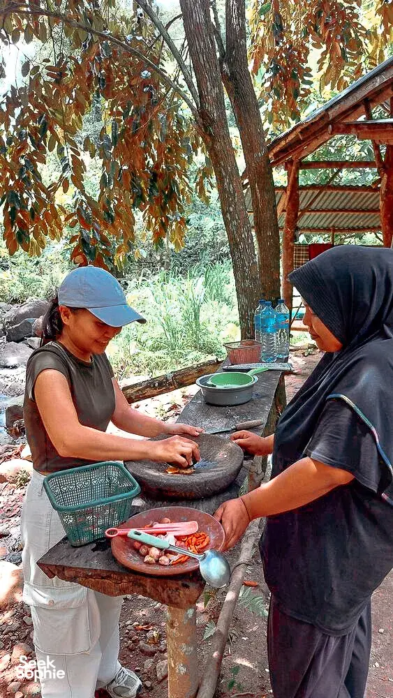 Former-logger forest walk cooking in Lombok: two people prep ingredients at a stone mortar table in the shade
