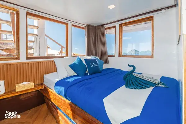 La Famille cabin on the Komodo boat with a blue bed, window views and a folded-towel swan, for 3D2N stays in Labuan Bajo