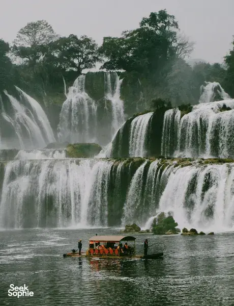 Cascading waterfall in Cao Bang with a small boat floating on the river below, Ha Giang Expeditions motorbike tour