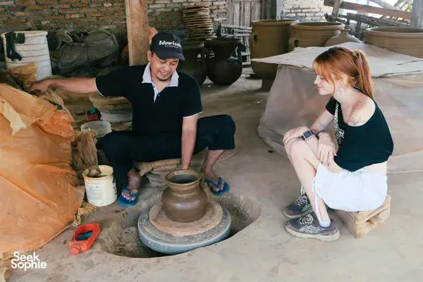 Attendees learning pottery techniques with local artisans, seated around a clay wheel in a Yogyakarta pottery village workshop