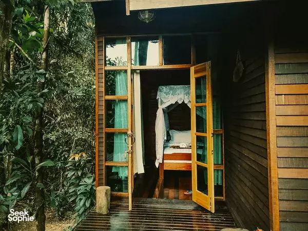 Open doorway to a wooden cabin at Scenic Riverside Resort, Sandakan, with lush greenery beyond for a stay along the Kinabatangan River