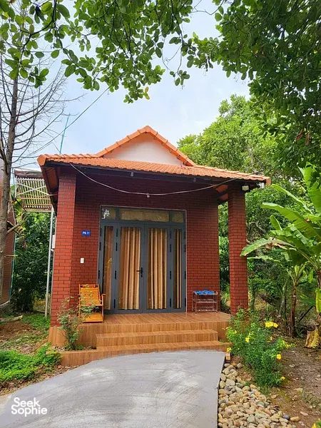 Red-brick bungalow with an orange-tile roof and covered entrance in the garden of Thuy Tien Eco Lodge, Cat Tien