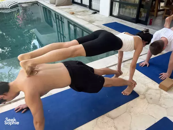 Practitioners hold plank and downward-dog variations on blue mats beside a private pool during a Bali yoga session, Canggu