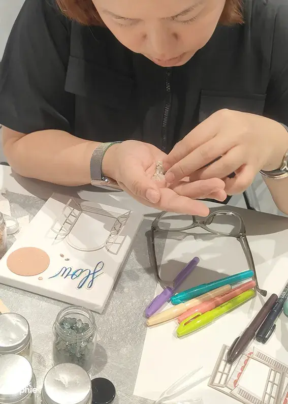 Close-up of hands assembling a vision board charm on a table of craft tools at Gemstory for birthday activities Singapore