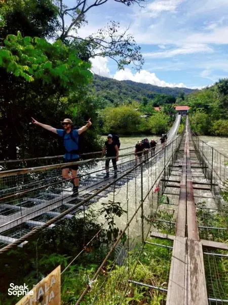 Hikers crossing a wooden suspension bridge over a river gorge during an Outreach Borneo jungle adventure near Kota Kinabalu