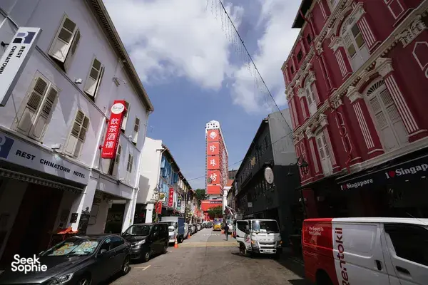 Singapore Chinatown street with shopfronts, parked cars and red heritage buildings, as a team explores alleys to find Singapore hidden gems