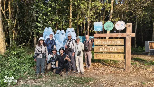 Group of travellers and local guides posing beside a wooden Ramsar sign in a forest in Cat Tien on a private ethical wildlife tour