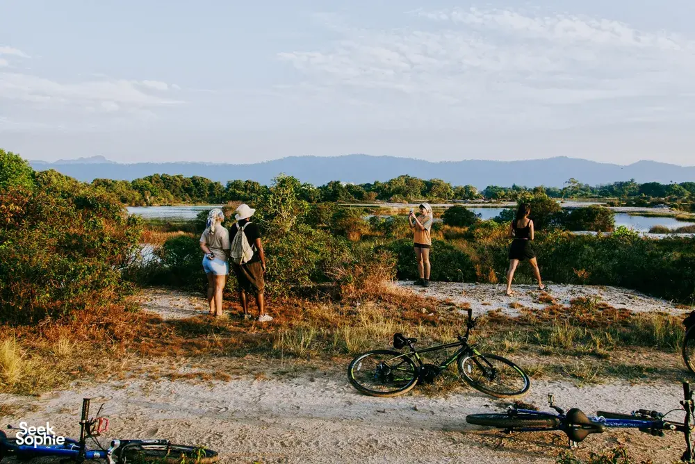Gravel track cycling in Langkawi: travellers walk with bicycles along the riverbank as bikes rest in the foreground